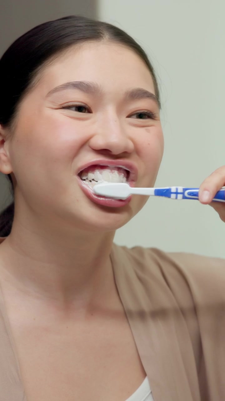 Young Woman Brushing Her Teeth in Front of a Mirror