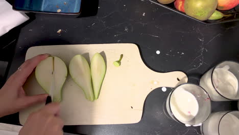 top view the girl is holding a knife in her hand and cutting a pear on a wooden board