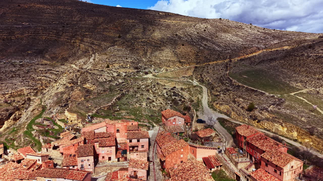 Vista panorámica de un pequeño pueblo en una zona montañosa durante el día con cielos nublados y terreno rocoso visible al fondo
