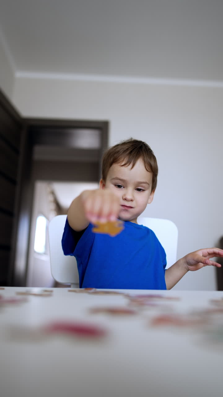 Adorable joyful kid claps hands looking at desk with puzzles. Lovely baby boy plays educational game at home. Vertical video.