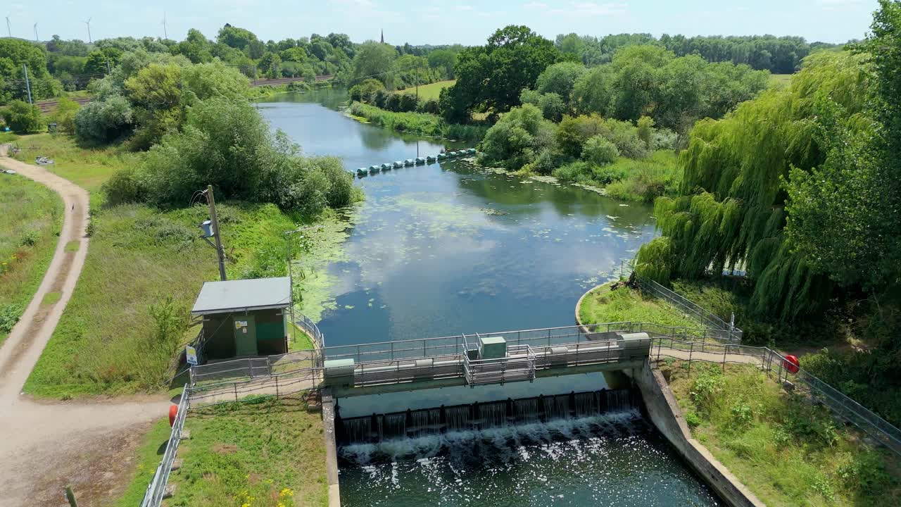 Cinematic drone view of tranquil English wetland habitat with river barrier and lush greenery in summer
