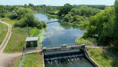cinematic drone view of tranquil english wetland habitat with river barrier and lush greenery in summer