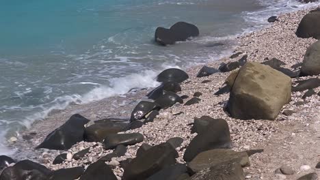Rounded-carved-black-stones-decorate-the-special-beach-with-pebbles,-washed-by-sea-waves-in-Mediterranean-coastline-of-Albania