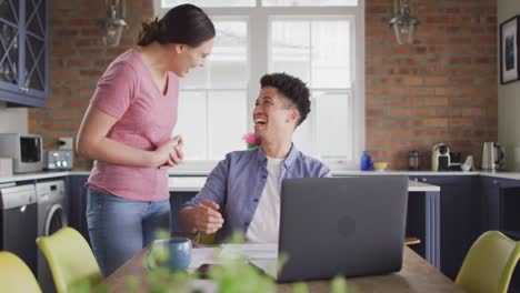 Glückliches-Gemischtrassiges-Paar,-Das-Mit-Einem-Laptop-Am-Tisch-In-Der-Küche-Sitzt