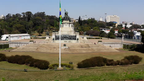 aerial shot approaching the independence monument passing trough the brazilian flag in the foreground with the ipiranga museum in the background of the scene