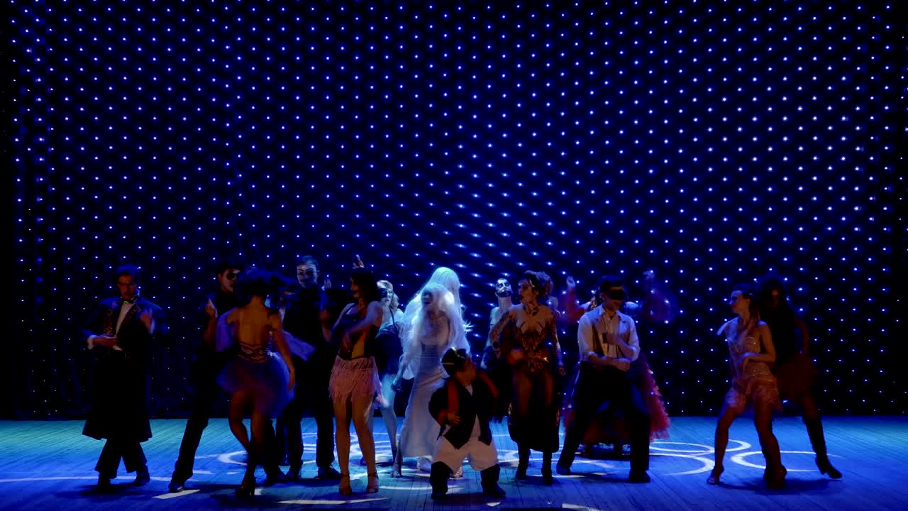 장면적인 의상을 입은 특별한 사람들이 극장의 무대에서 춤을 추고 있습니다.