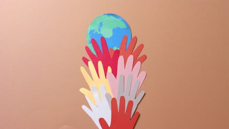 close up of hands together with globe made of colourful paper on brown background with copy space