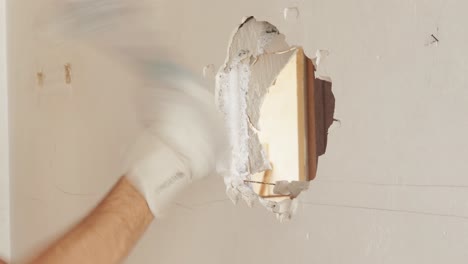 Hand-breaking-white-wall-with-sledge-hammer-making-a-hole,-close-up-shot