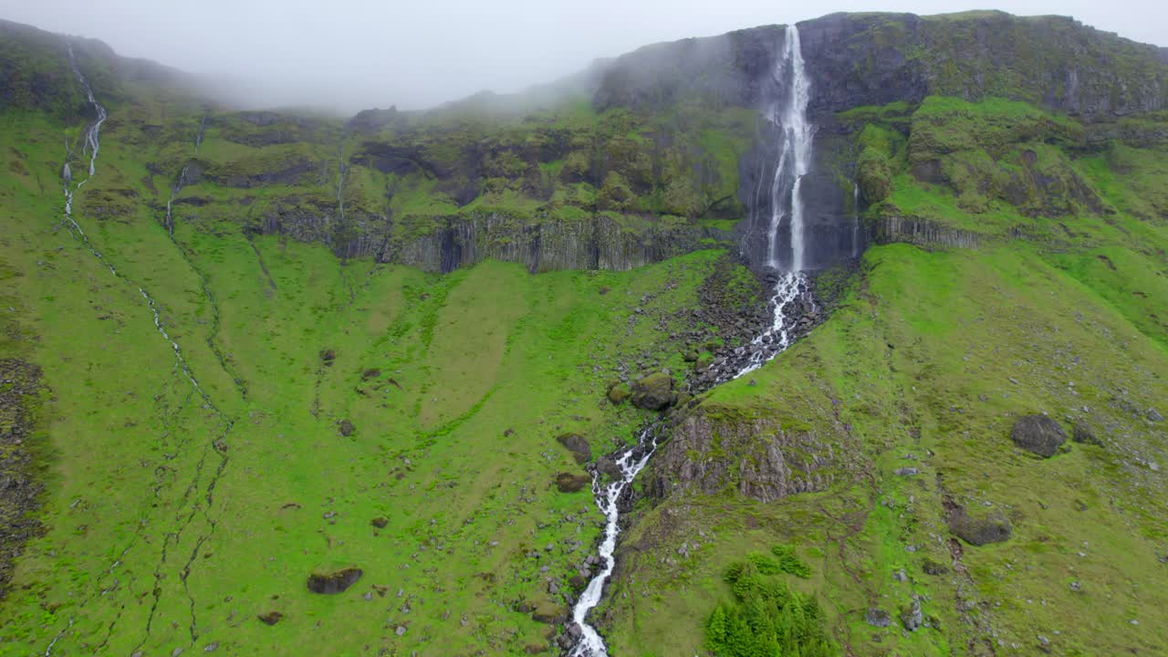 cascada que fluye hacia un estrecho arroyo de montaña con hierba verde