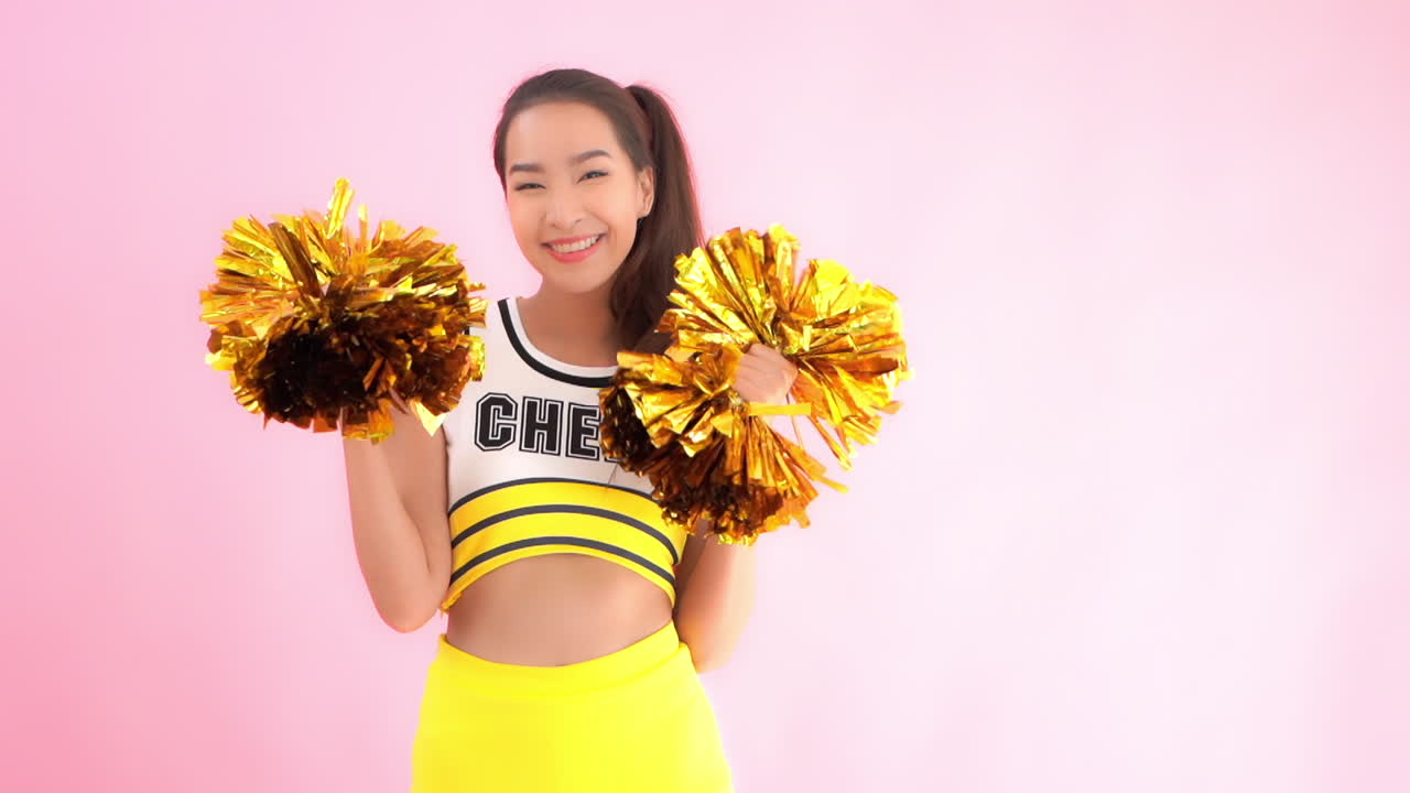 Dressed in the school colors or yellow and brown a cheerleader raises her pom-poms in a cheer and smiles