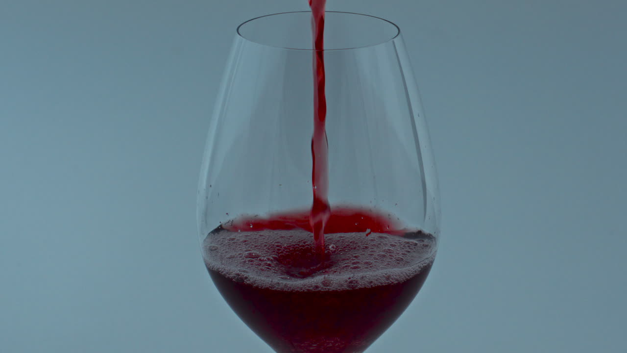 Liquore gourmet limpido che scorre nel calice, primo piano. Vino rosso che scorre nel bicchiere.