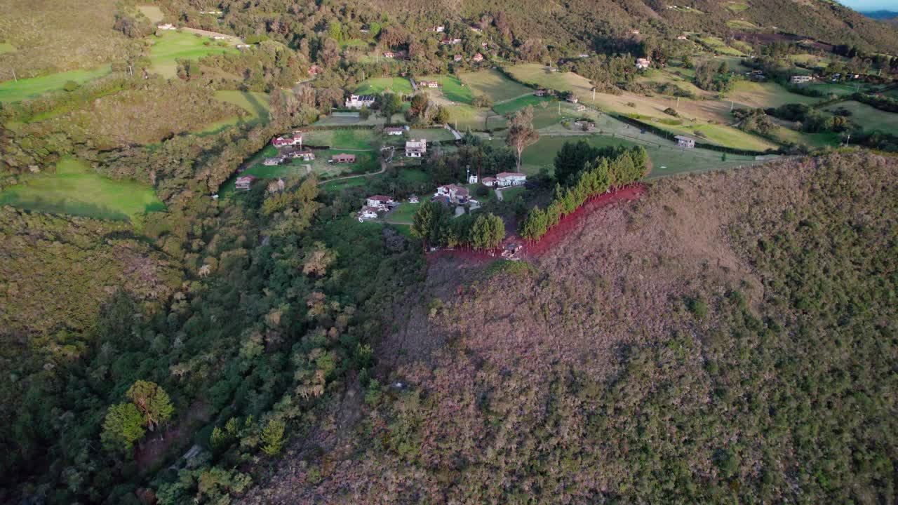Zoom in aerial shot revealing rural homes over forested hills in Guatavita, Colombia during golden hour