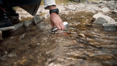 Primer-Plano:-Un-Hombre-Recoge-Agua-En-Un-Termo-De-Un-Río-De-Montaña-Durante-Una-Caminata