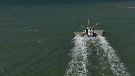 large trawler fishing boat, trawling large nets, block of seagulls flying behind boat, wide angle drone slow motion, following behind boat