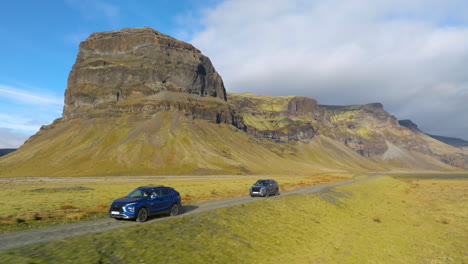 vehicles driving with the view of lómagnúpur mountain in background in iceland - aerial pullback