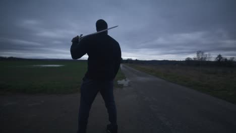 Modern-Black-Swordsman-Warrior-Awaiting-Battle-Opponent-in-Open-Field-Under-Grey-Sky,-Europe,-4K-|-Muscular,-Intimidating,-Shadow,-Figure,-Blurry,-Dark-Clothes,-Powerful,-Turning,-Weapon-Pull