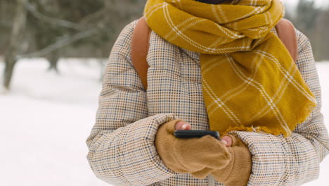 nahaufnahme einer frau, die im winterwald smartphone und herumschaut