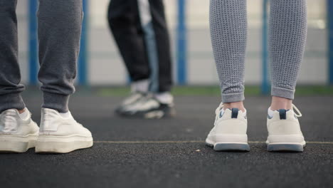 leg view of three athletes in joggers and sneakers walking on court with a blurred background, another athlete's leg is visible in joggers and sneakers, walking in the same direction