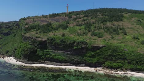 pan right shot of the vietnamese flag atop a cliffside tower surrounded by forest and beach under bright sun