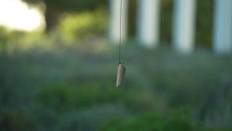 close up shot of a pendant on a string gently moving in the breeze with blurred background