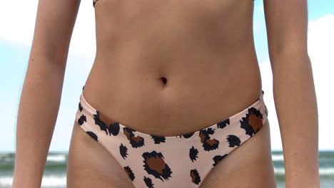 close-up of a slim belly of a young healthy woman in bikini at the ocean beach