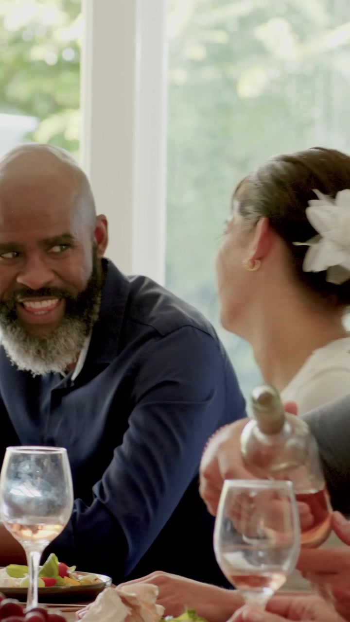 Woman raising wine glass, guests clapping and passing glasses while celebrating meal