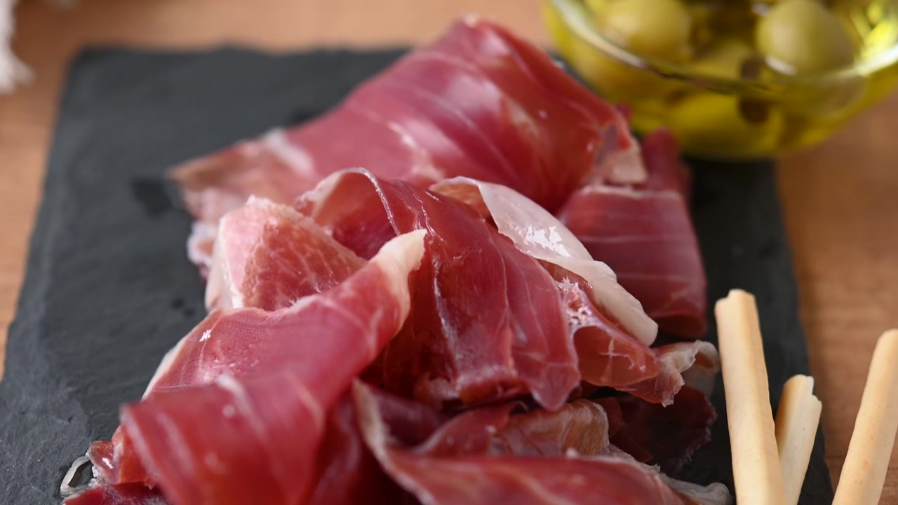 Fette di prosciutto Serrano servite con grissini e olive verdi