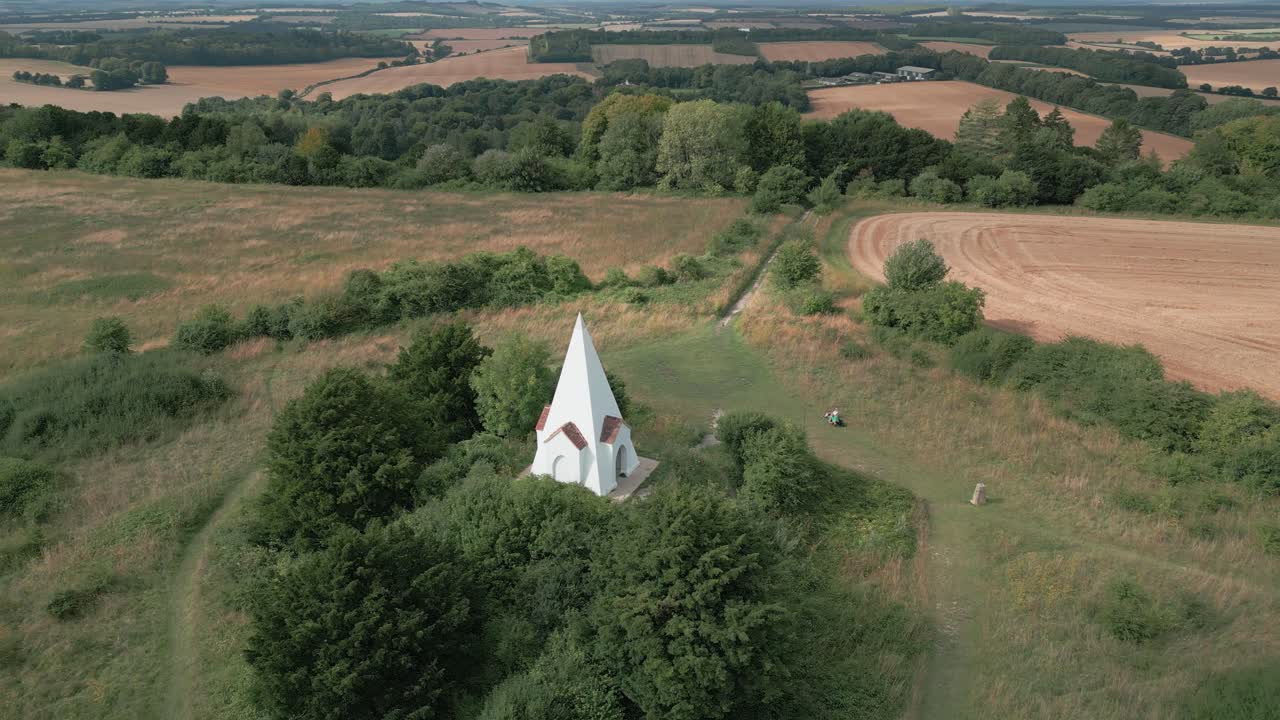 Aerial orbit of Farley Mount Monument, Winchester, UK, surrounded by fields and scenic countryside, white building in lush green hills