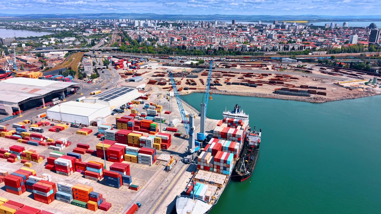 Burgas, Bulgaria, 21 May 2026: Container ship docked at cargo terminal, port of Burgas, Bulgaria. Colorful shipping containers, blue cranes and scrap metal yard with city in background.