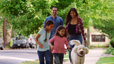 Family-Walking-Dog-Along-Suburban-Street