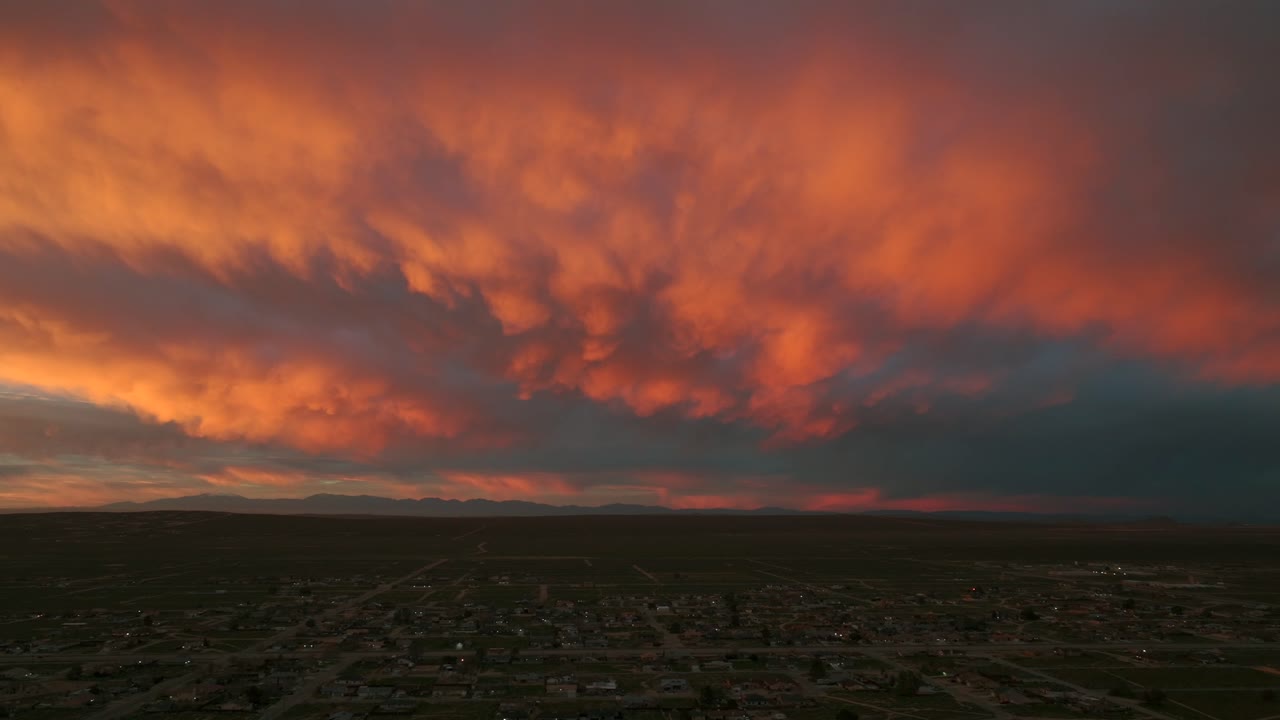 Drone shot overlooking California City at sunrise as the camera slowly pans left. Warm red and orange clouds fill the sky, creating a calm atmosphere of a city awakening, suitable as a background
