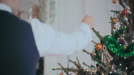 man hanging red bauble on illuminated christmas tree