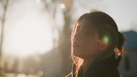 a close-up of a girl walking with her hair covering her face, expressing a deep sense of grief. the soft backlighting from the sunset enhances the emotional and reflective atmosphere