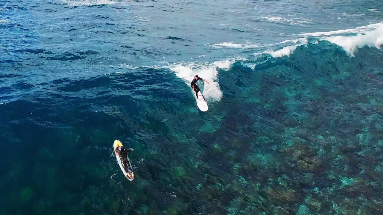 Aerial overview of longboard surfer hanging five on nose of surfboard over shallow reef