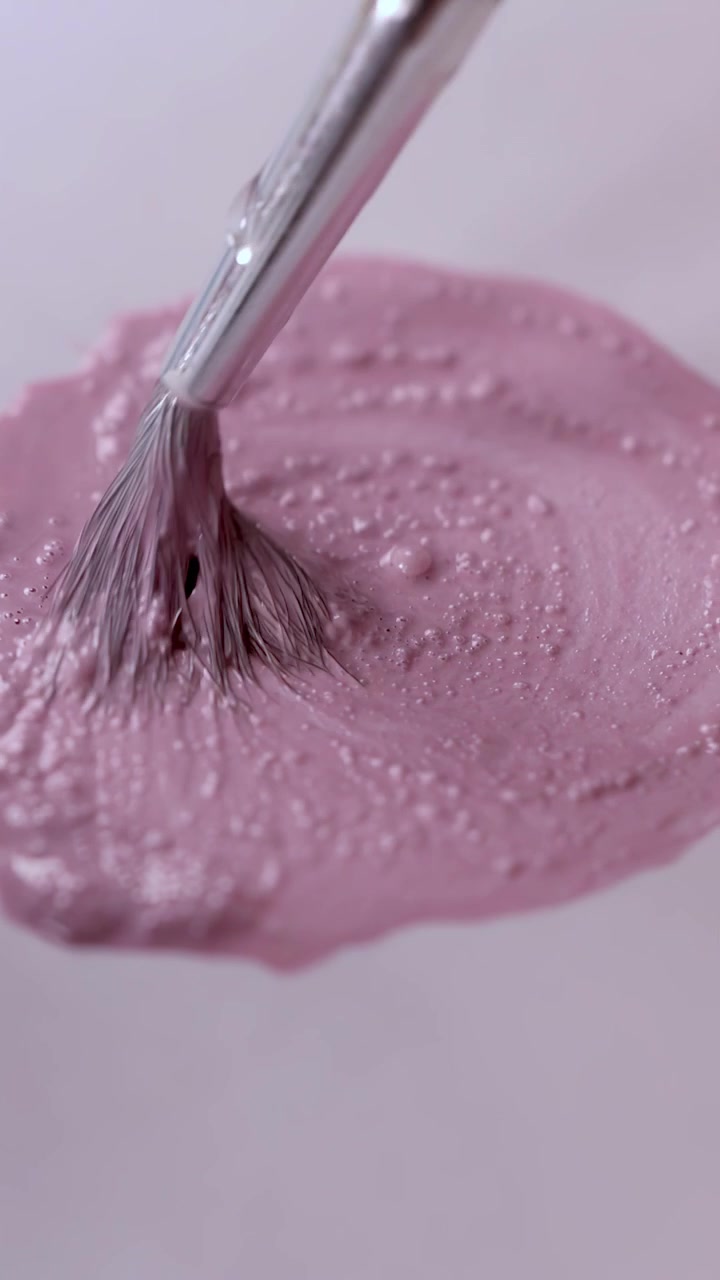 Palet üzerinde pembe boyayı karıştıran fırçanın yakın çekimi, yumuşak aydınlatma, akıcı kamera hareketi, sanatsal süreç.
