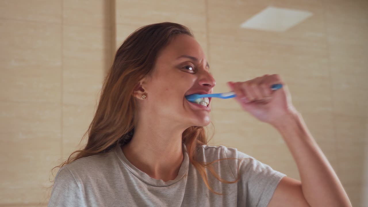 Young woman brushing her teeth happily in front of the mirror