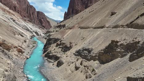 aerial drone shot showing a vivid blue river cutting through mountainous terrain near a traditional monastery.