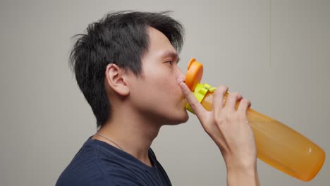 thirsty young chinese male drinks water from coloured transparent bottle