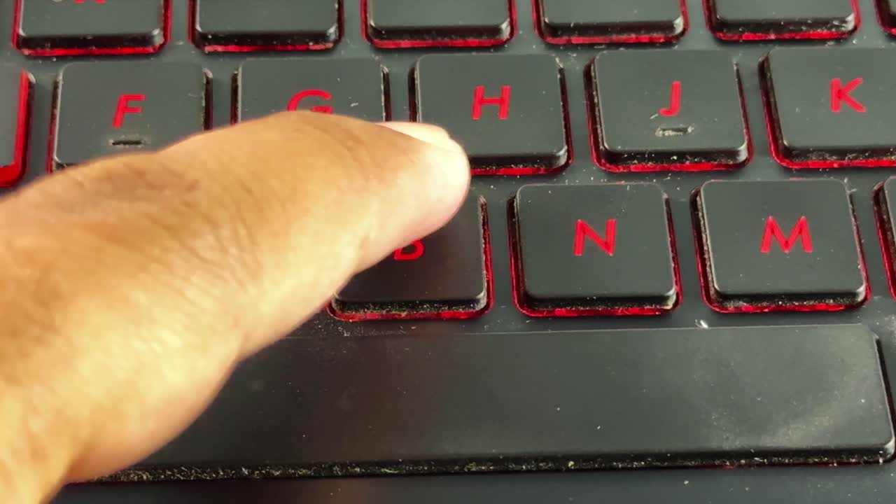Nærbillede af en finger der taster på et rødt baggrundsbelyst laptop-tastatur, specifikt på "B"-knappen, ideelt til temaer som teknologi, kontorarbejde og digital kommunikation.