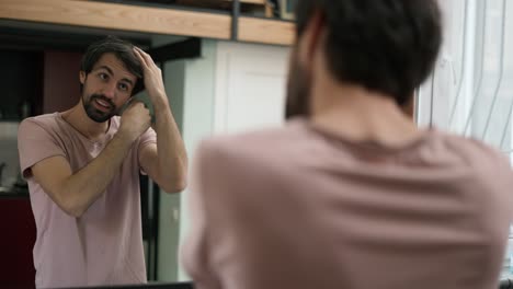 handsome young man combing hair in mirror, put on headphones getting ready to go out