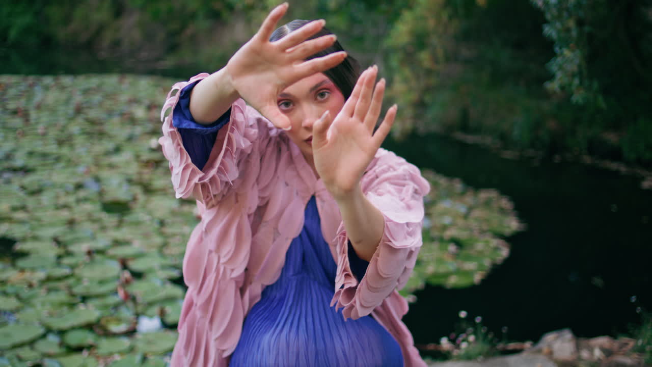 클로즈업 판타지 소녀는 카메라를 보고 자연 연못에서 손을 움직여 매료시니다.
