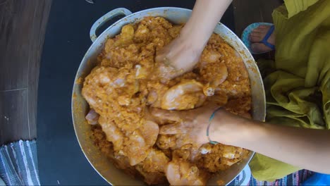 raw chicken pieces being marinated inside casserole pan by hand