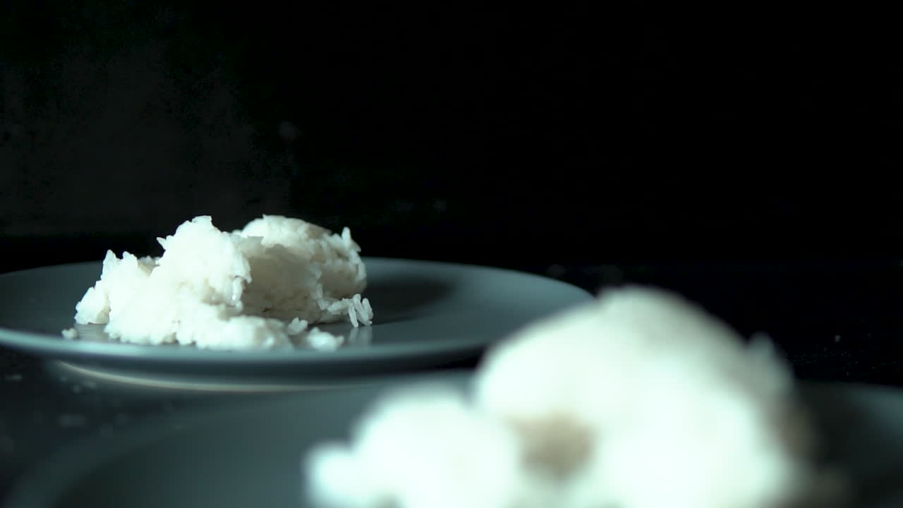 Steam floats over a portion of rice lying on a grey plate, slow motion smoked from meal