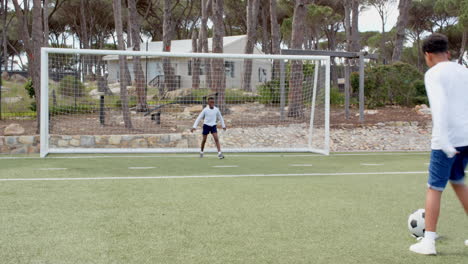 multiracial boys playing soccer on field, one kicking ball towards goal, enjoying game