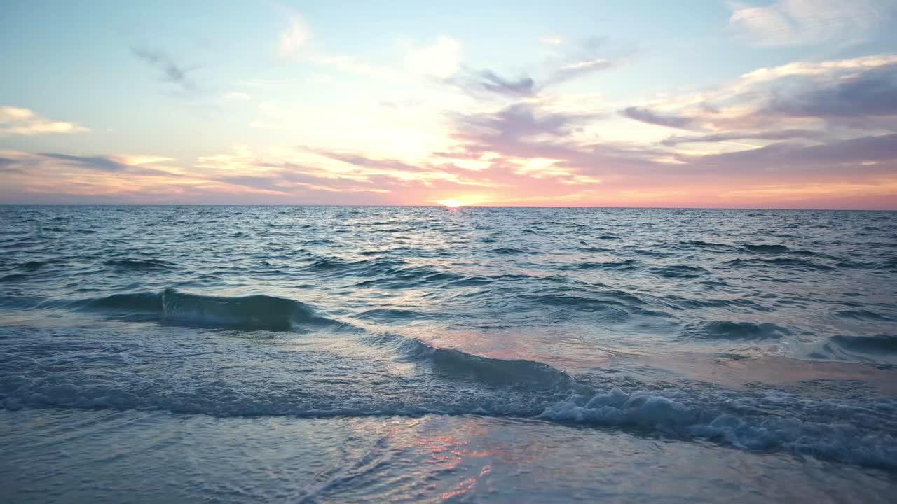 Gentle waves of the sea just after the sea has set on the horizon on a beach in Florida. Beautiful blue waves lap on the shore with a orange tinged in the clouds .