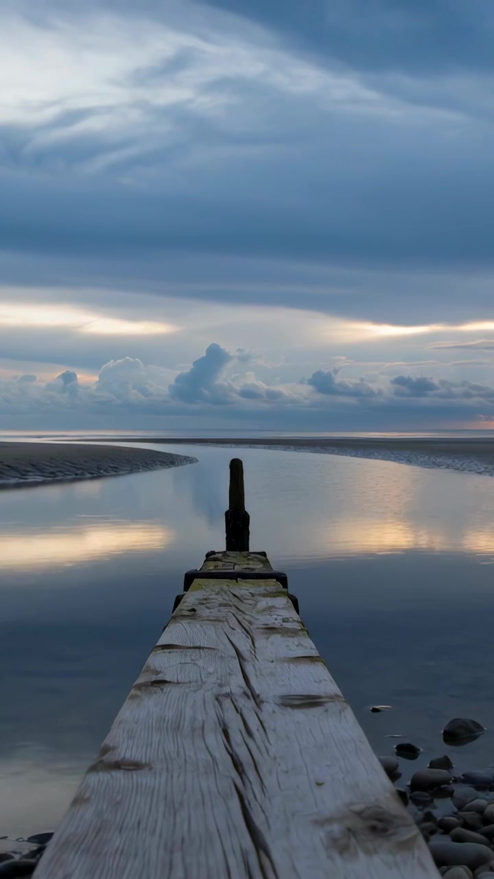 Vertical video: Showing wooden jetty at inlet, horizon light rising, clouds drifting, post standing
