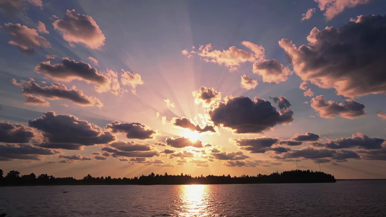 A stunning sunset video captures the sun's rays piercing through scattered clouds over a serene