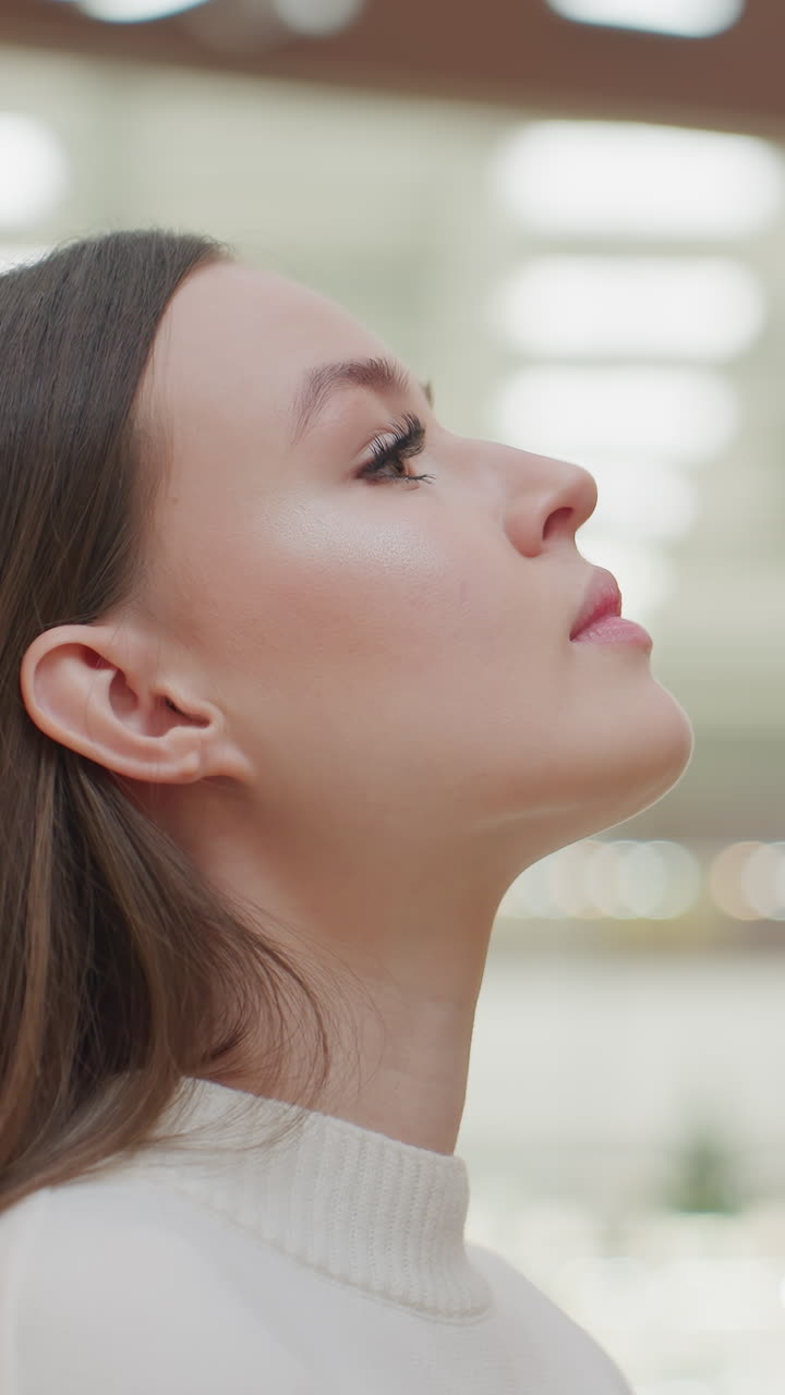 Calm lady walking up to Christmas tree, gazing at it peacefully while another shopper passes by in bright, well-lit mall, festive atmosphere with warm lighting, holiday decorations in background
