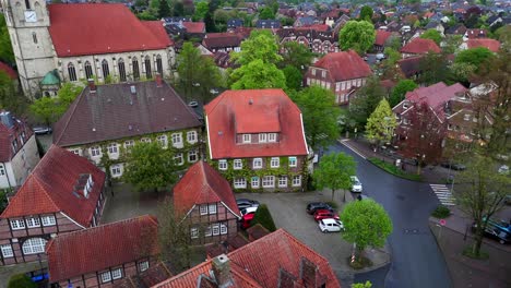 historic church and old houses with green plants on wall. cloudy day in spring. aerial lateral wide shot. parking cars in center of town.