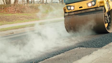 compactor driving over the hot and steaming asphalt on the road at a construction site